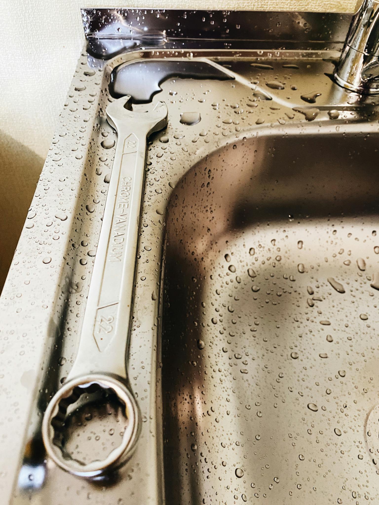 Close-up of a metal wrench on a stainless steel sink with water droplets.