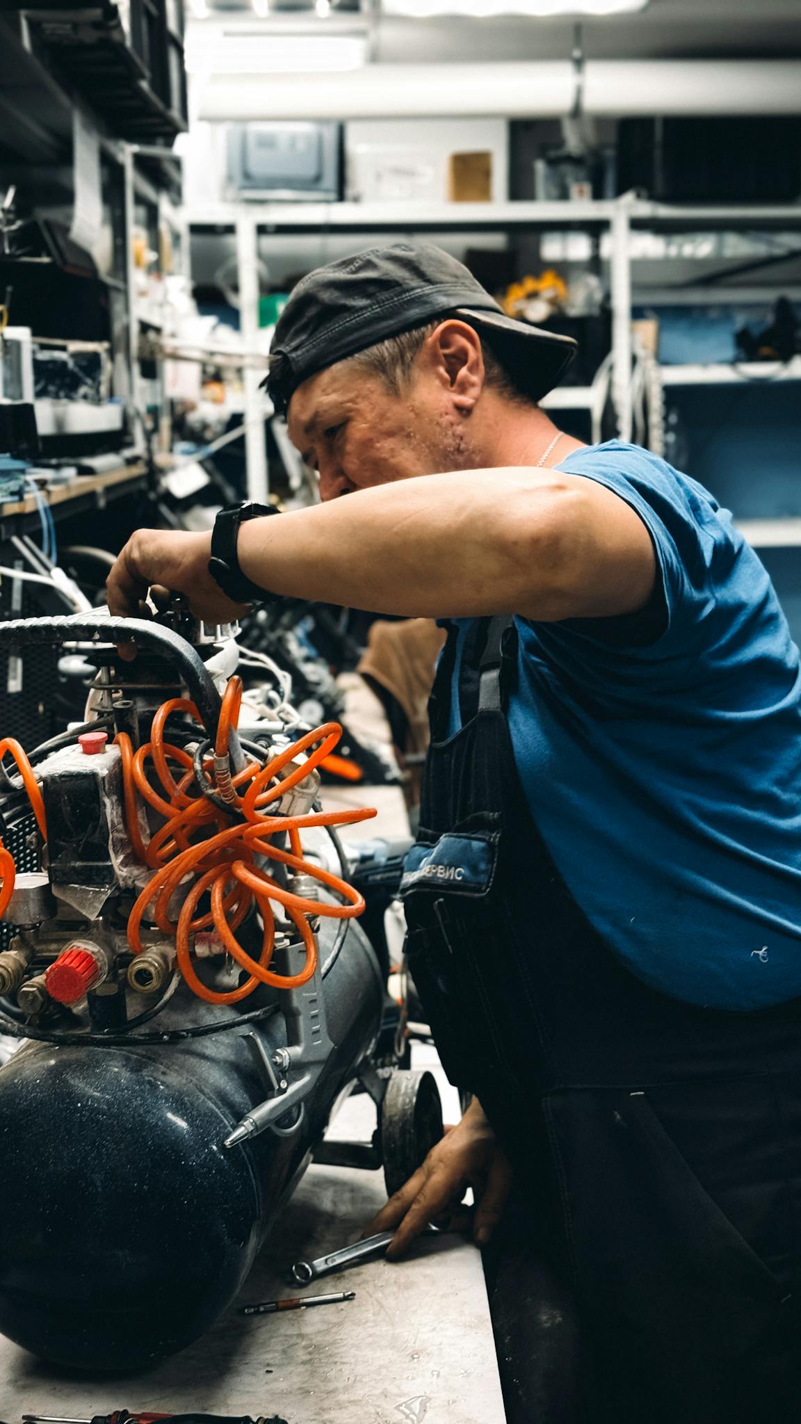 Skilled mechanic repairing air compressor in a cluttered workshop setting.